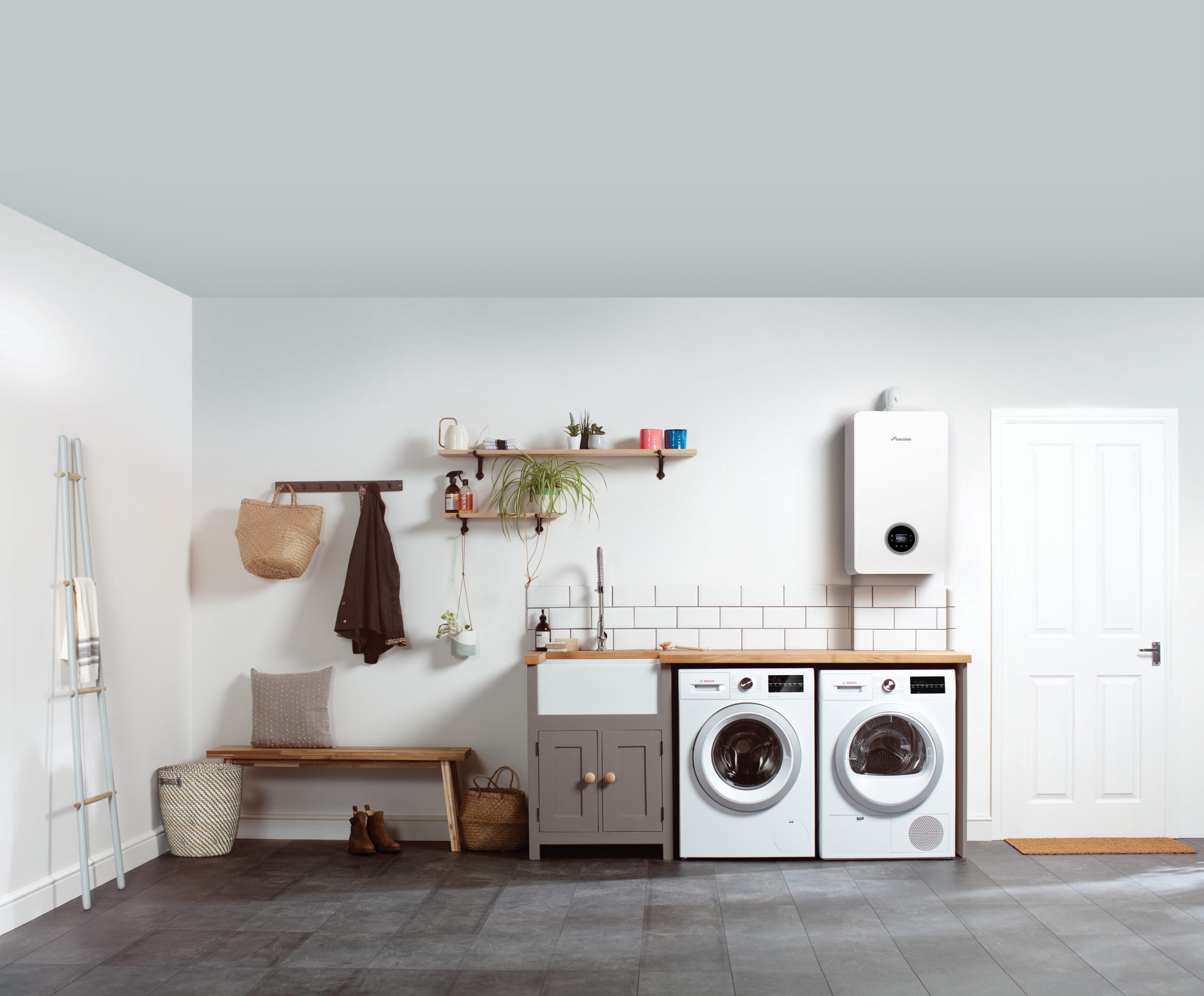Modern utility room featuring a white boiler mounted on the wall, alongside a washing machine and dryer, wooden countertop, sink, and various storage elements, illustrating efficient home heating solutions.